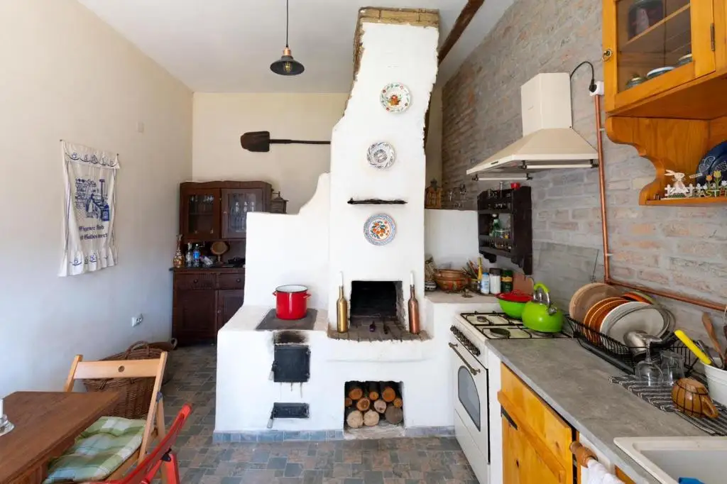 Guest kitchen with a whitewashed traditional masonry hearth, exposed brick wall, copper pipes and hand-painted plates