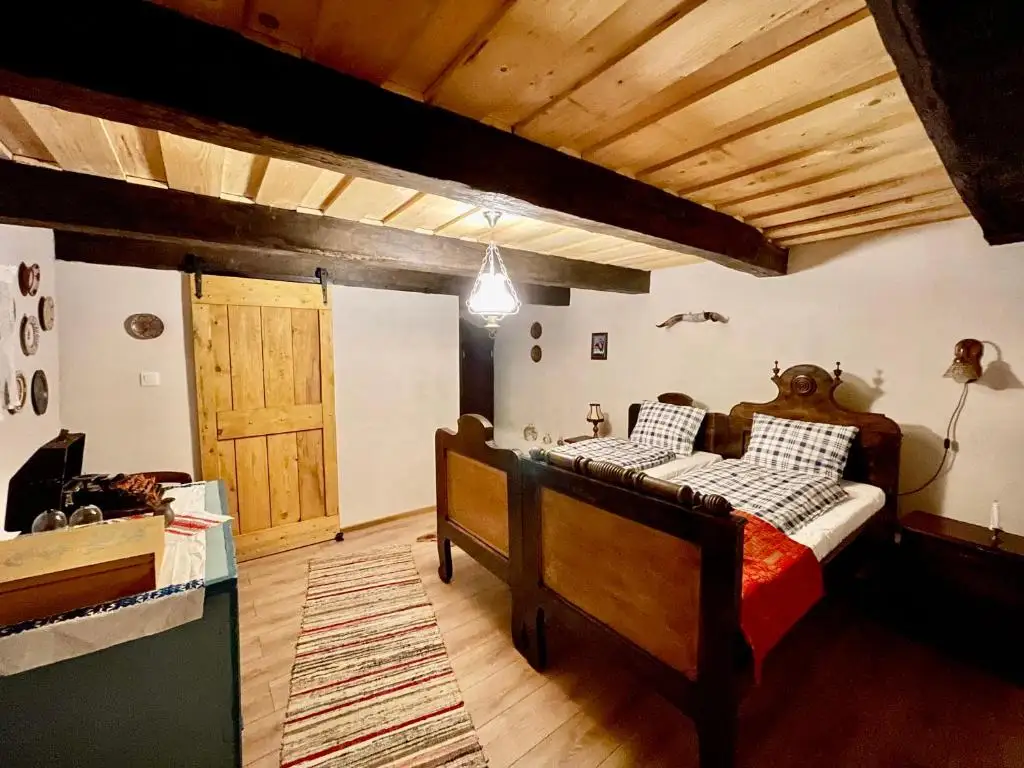 Rustic bedroom with heavy timber ceiling beams, antique wooden beds with a red wool blanket, and a sliding barn door