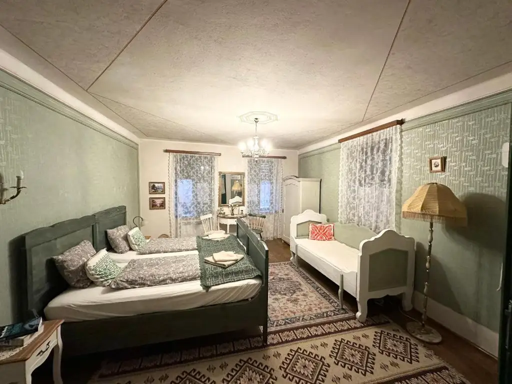 Sage-green bedroom with two beds and a daybed, lace curtains, patterned wall panels and kilim rugs