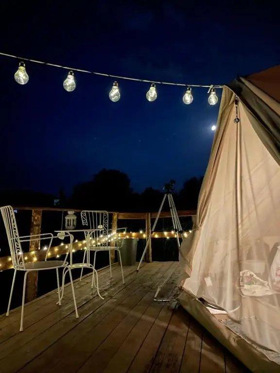 Bell tent on its wooden deck at night under a string of warm lights, with the moon low in the sky